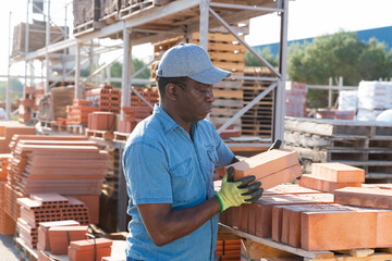 Shop assistant man is checking quality of bricks in the open area of a construction store