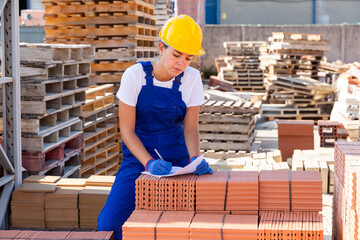 Young woman working in construction material storage. She's writing something on sheet of paper...