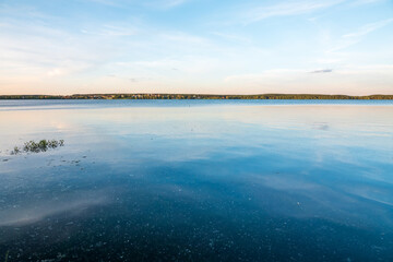 Lake with pine and birch forest on the shores at summer or early autumn sunset.