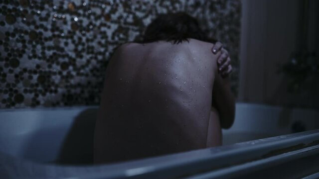 a girl sits in a bathroom with a wet back in a gloomy setting. despair fear or addiction concept