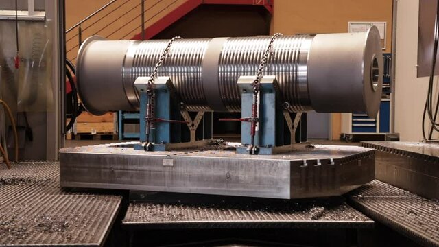 Rotating big metal cylinder chained down on machine at workshop.