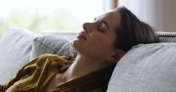 Close up side view face of sleeping on sofa woman. Serene beautiful female relaxing in living room or hotel, breath fresh conditioned air inside, enjoy modern house, leisure at home, no stress concept