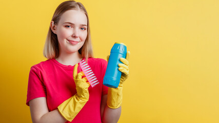 Young blonde happy smiling woman ready to cleaning house with household supplies isolated over yellow color background. Woman Portrait with cleaning brush cleaner in rubber gloves. Long web banner.