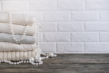 Stack of white cozy knitted sweaters and beads on a wooden table.