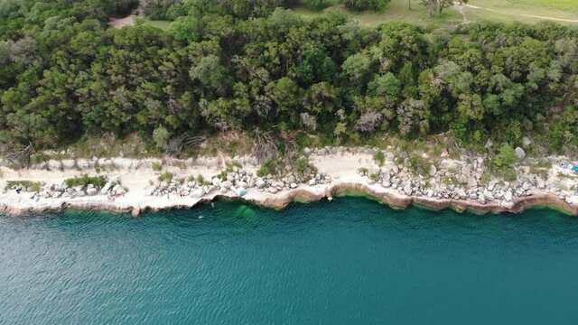Aerial panning shot showing Cayon Lake Shoreline and green forest trees in background - Texas,America