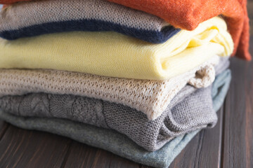 Cozy sweaters in autumn colors on brown wooden background.