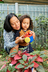 Mother explaining little son how to hold watering can when water plants and flowers in house...