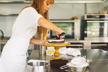 Confectioner girl is preparing a cake biscuit with white cream and chocolate. Cooking cakes.