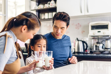 Obraz na płótnie Canvas Portrait of enjoy happy love asian family father and mother with little asian girl smiling and having breakfast drinking and hold glasses of milk at table in kitchen