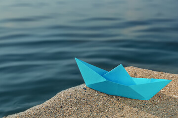 Light blue paper boat near river on sunny day, space for text