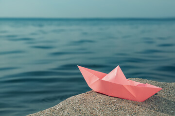 Pink paper boat near river on sunny day, space for text