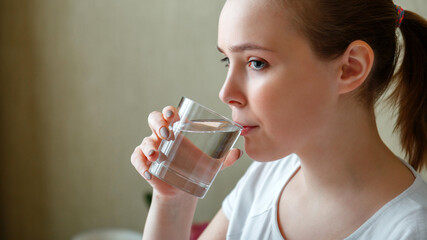 Young woman drinks glass of pure water in morning after waking up. Happy teen girl maintains water balance for body health by drinking a transparent cup of clean water. Long web banner