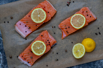 Three Row Salmon fish fillet uncooked with different spices and lemon slice on it on a backing paper.