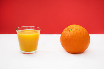 Glass of orange juice and large orange on read and white background