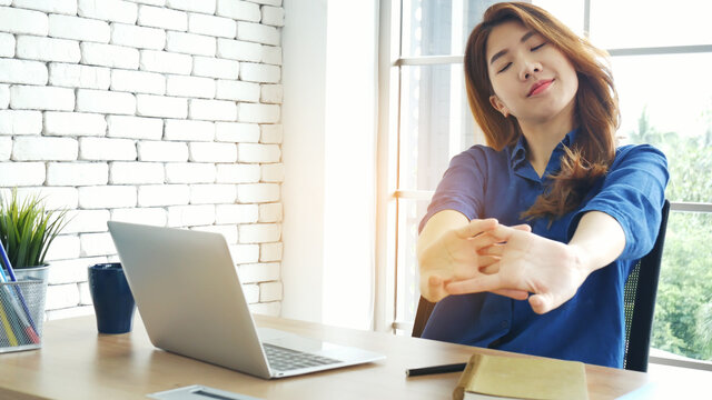 Woman streching arm raised sitting incorrect position home office desk. Back side of young asian woman tired from work body stress back pain office syndrome. Female work from home new normal concept