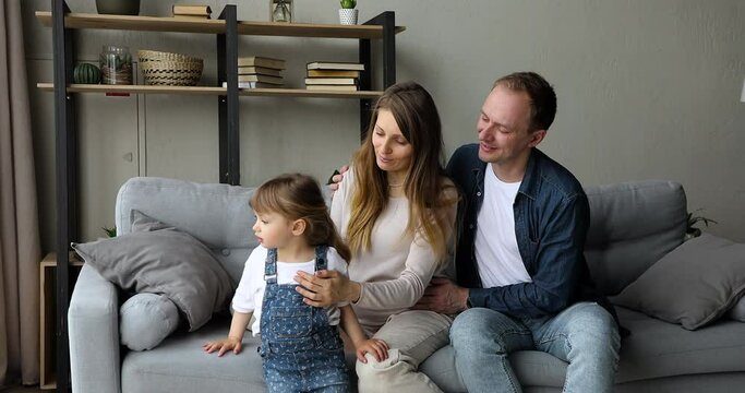 Loving pregnant of second child woman holding comb brushing hair of 4s little cute daughter, sit together on sofa with caring husband. Happy parenthood routine, communication, family bonding concept