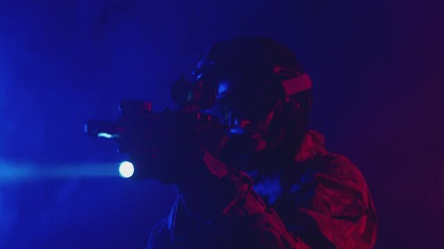 Military woman in uniform takes aim from rifle and illuminates flashlight the smoky terrain. Woman shines a weapon flashlight while standing in a blue-and-red-lit studio.