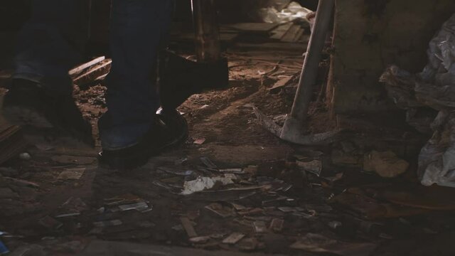 A man in jeans and heavy boots with an axe in his hand walks slowly through an abandoned house. The concept of a maniac looking for a victim