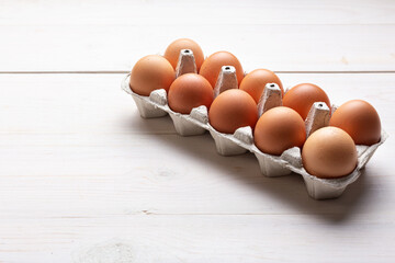Fresh organic chicken eggs in carton pack or egg container  on white wood background.