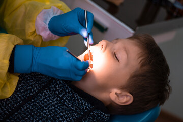 Boy 7-11 in the dentist's chair and the doctor's hands in blue gloves during dental examination or...