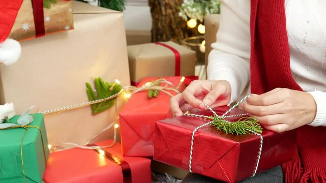 Close up woman hands wrap present gift in cozy living room. Woman wrapping christmas gift box under xmas tree. Asian woman decor bauble ball christmas tree in xmas holiday winter seasonal celebration