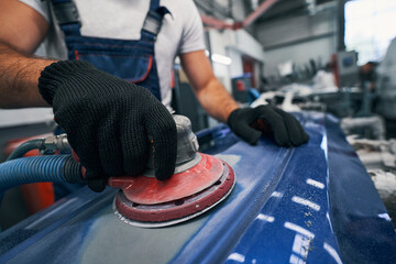 Repair shop worker sanding car with grinding machine