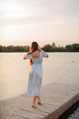 Anonymous woman with long hair in blue dress on the pier in sunset  - 455220298