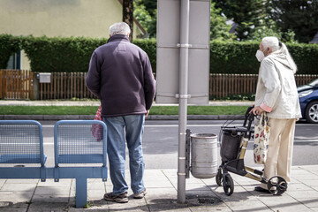 two old people wearing a mask and waiting for the bus on a station in Munich