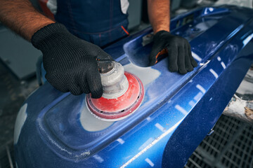 Mechanic using grinding unit on blue bumper