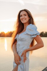 Happy young woman in front of river and sunset sky  - 455220677