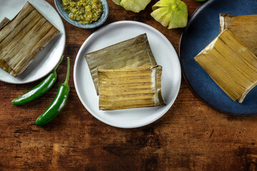 Tamales oaxaquenos, traditional dish of the cuisine of Mexico, various stuffings wrapped in green leaves, overhead flat lay shot. Hispanic food on a rustic wooden background