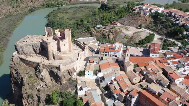 Scenic aerial view of medieval Cofrentes Castle towering over city residential buildings atop rocky cliff over Cabriel River, Valencia, Spain. High quality 4k footage