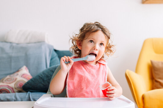 Cute funny baby girl 2 years old sitting with a spoon in his mouth.