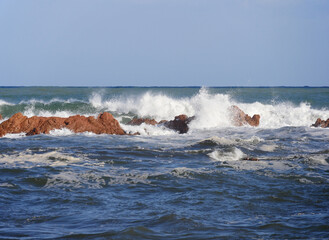 Brandung an der Küste am Strand von la Spiaggetta, die sich durch die Anwesenheit des typischen rötlichen Porphyrs auszeichnet, der sich in transparentem und kristallklarem Wasser widerspiegelt.