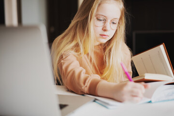 Portrait of young girl doing her school work with laptop writing with a pen in a notebook