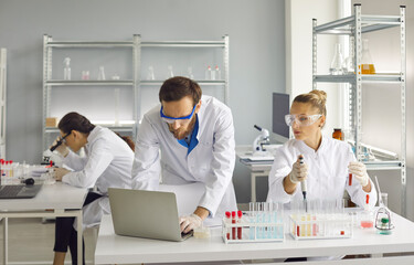 Scientists are doing important research. A woman holds a test tube, a man works at a laptop....