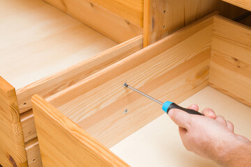 Young adult man hand using manual screwdriver and screwing screw in board of opened drawer for rail...