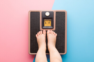 Baby barefoot standing on weight scales on light pink blue floor background. Pastel color. Closeup....