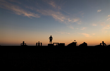Naklejka premium Silhouette of adult man looking at view on beach with fishing boat and winch during sunset