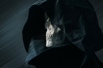 Mythical portrait of the image of death. Close up view skull in black hood, on dark background.