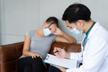 Fototapeta premium Professional psychologist male wearing protective medical face mask conducting a consultation and making notes while talking to stressful woman in face mask during coronavirus or COVID 19 outbreak