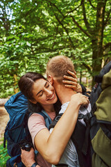 Happy couple with backpacks hugging in nature