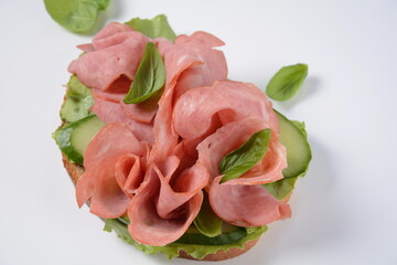 Open ham Sandwich with cucumbers, basil, and a crusty slice of rye bread and salami