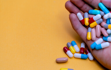 Hand holding colorful capsule pills on yellow background. Antibiotic drug overuse concept....