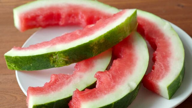 Watermelon peels on white ceramic plate. Man putting watermelon slices, rind on the plate. Video 4k resolution