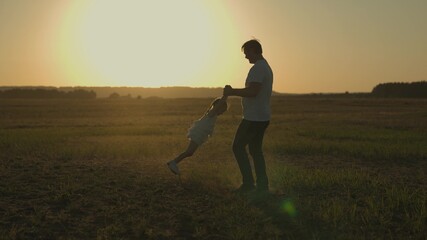 dad is circling little daughter at sunset, silhouette of father and child against sky, happy family, childhood dream, to love and play with kid, girl with parent is playing cheerfully, trip to nature