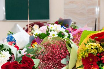 A bouquet of beautiful bright flowers on a school desk on September 1 against the background of a school board. Selective focus. Close-up