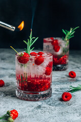 Raspberry lemonade in a glass with ice and fresh rosemary on a concrete background.