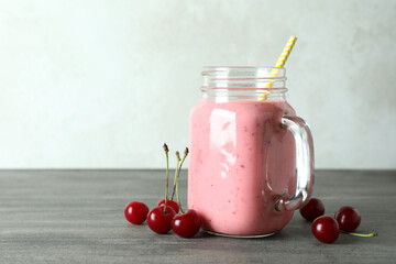 Glass jar of cherry smoothie and ingredients on gray textured table