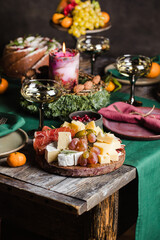 Decorated Christmas table served for 3 persons. Cheese plate with grape, ham, candle, cake.